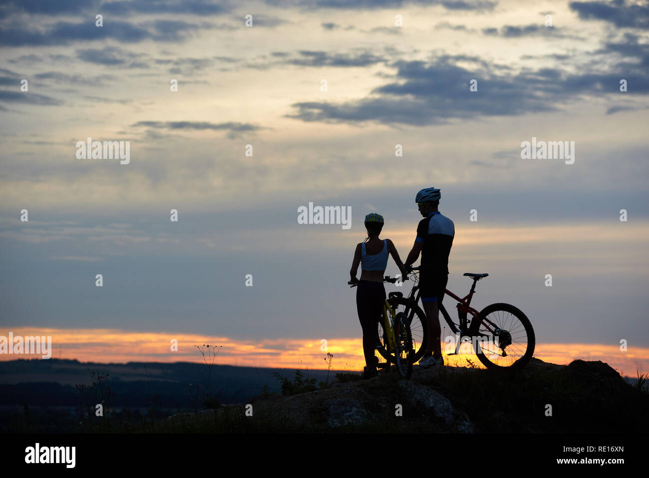 Ansicht der Rückseite zwei junge Menschen mit Mountainbikes stehen auf einer Klippe mit schönen Landschaft von Hügeln und Himmel bei Sonnenuntergang. Das Konzept einer gesunden Lebensstil Stockfoto
