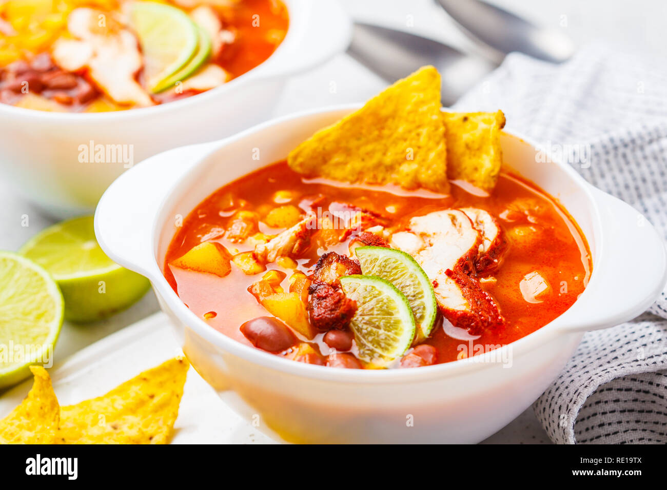 Mexikanische Suppe mit Bohnen, Hühnchen, Mais und Nachos in weißen Schalen. Chili con Carne - traditionelle mexikanische Küche. Stockfoto