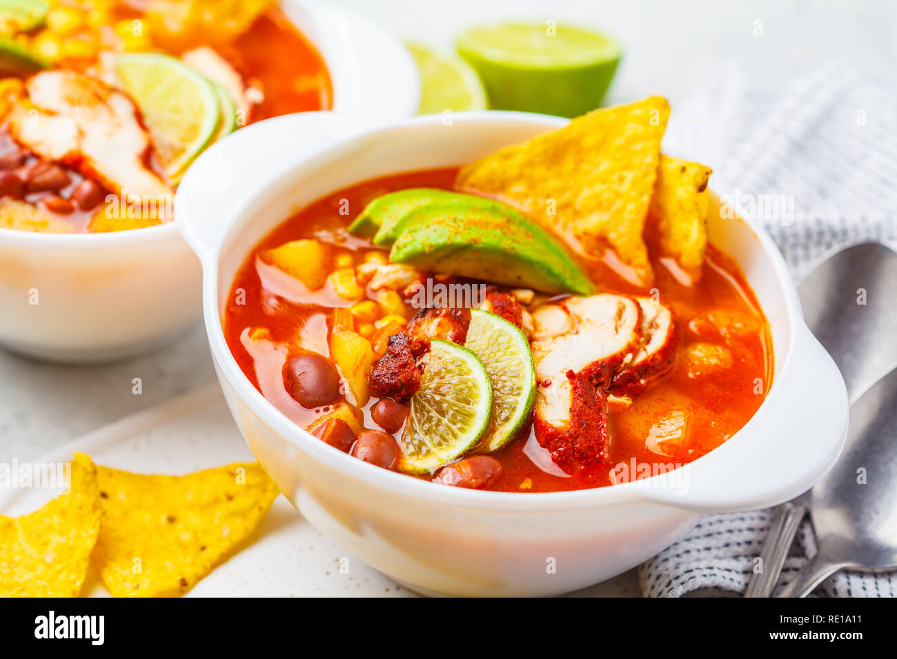 Mexikanische Suppe mit Bohnen, Hühnchen, Mais und Nachos in weißen Schalen. Chili con Carne - traditionelle mexikanische Küche. Stockfoto