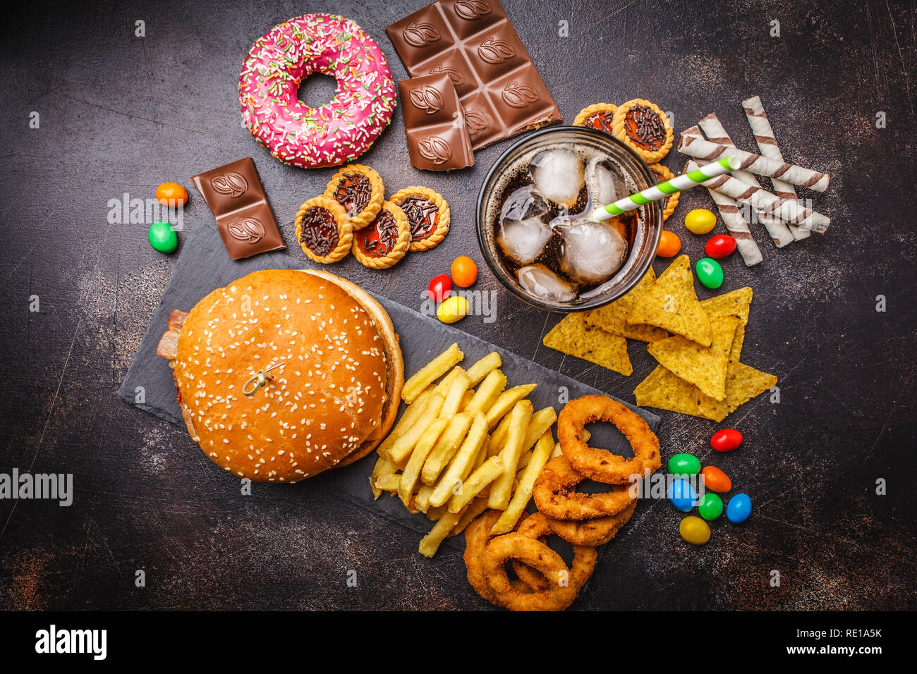 Junk food Konzept. Ungesunde Lebensmittel Hintergrund. Fast Food und Zucker. Burger, Süßigkeiten, Chips, Schokolade, Donuts, Soda auf einem dunklen Hintergrund. Stockfoto