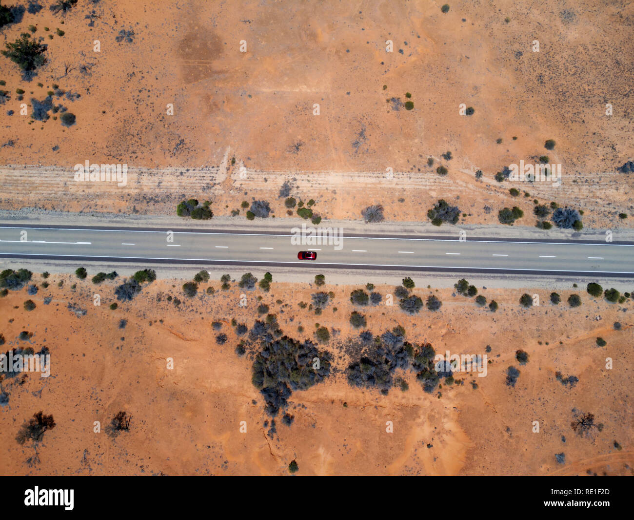 Aus der Vogelperspektive eines einsamen roten Autos, das auf einer geraden Straße durch eine Wüstenlandschaft fährt Stockfoto