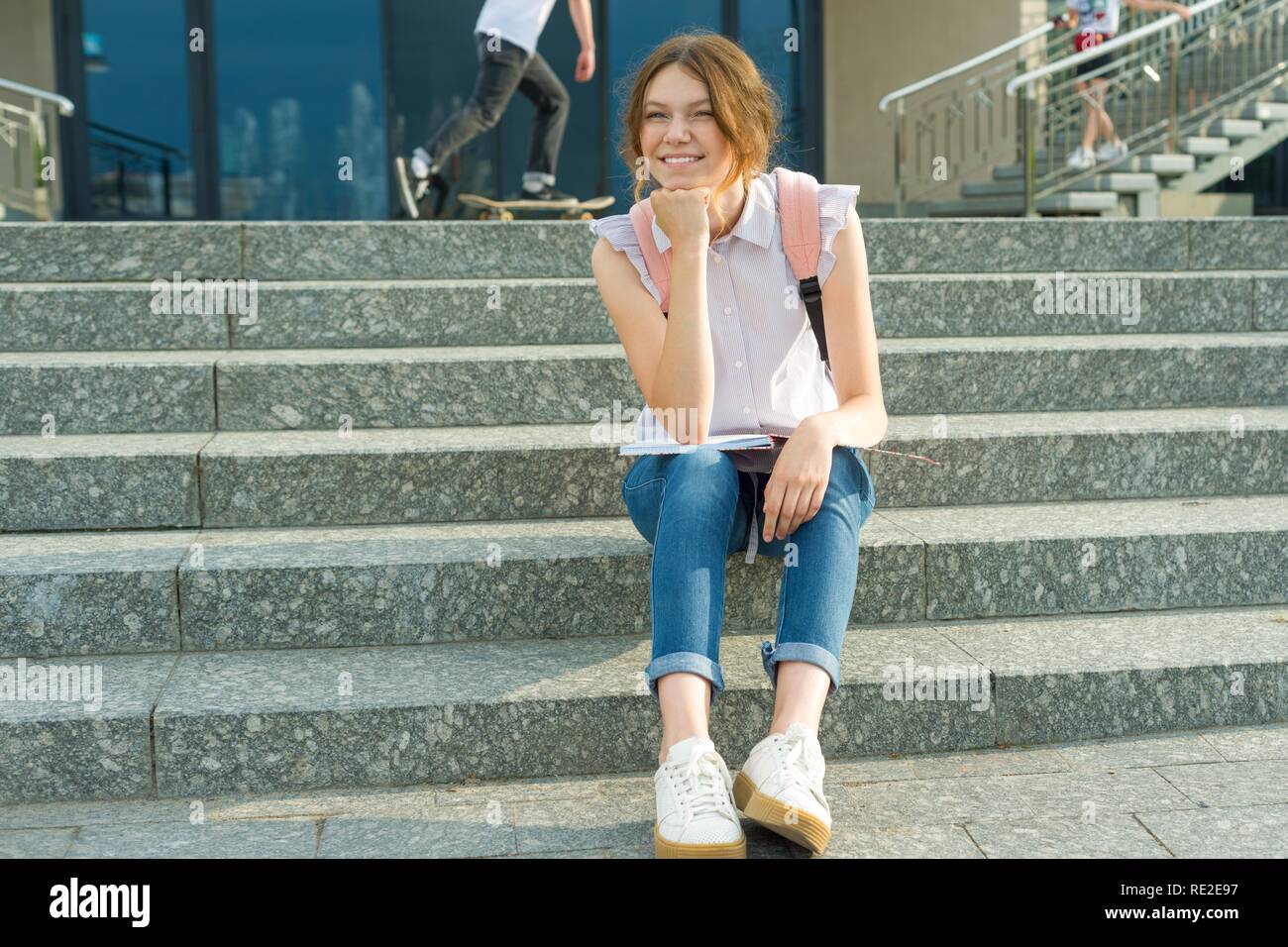 Outdoor Porträt der 14-jährigen Schülerin. Junges Mädchen mit Rucksack, sitzt auf der Treppe hält School Notizbuch in der Hand Stockfoto