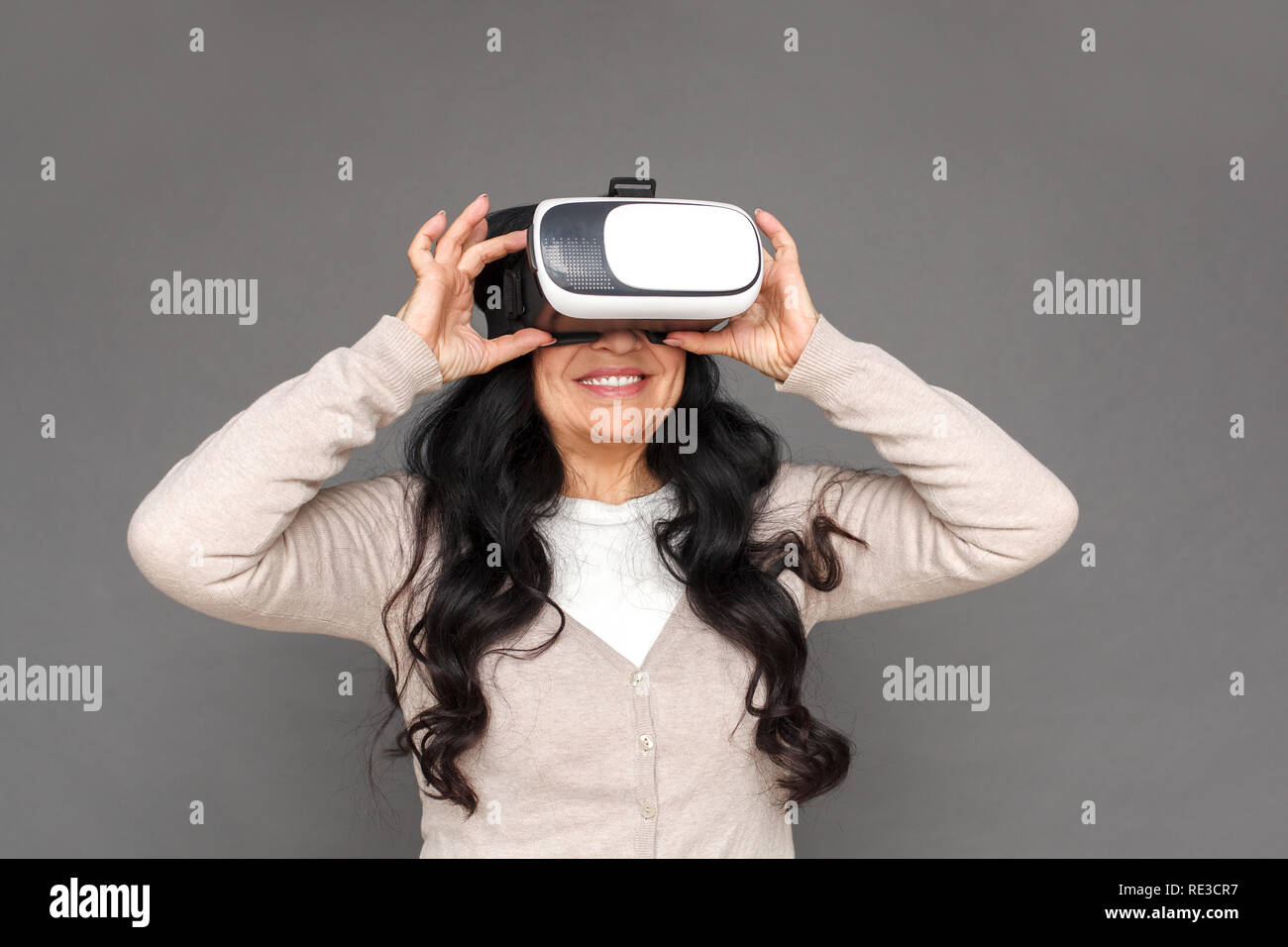 Freestyle. Reife Lady in der Virtual reality Headset stehen isoliert auf grau Video begeistert Stockfoto