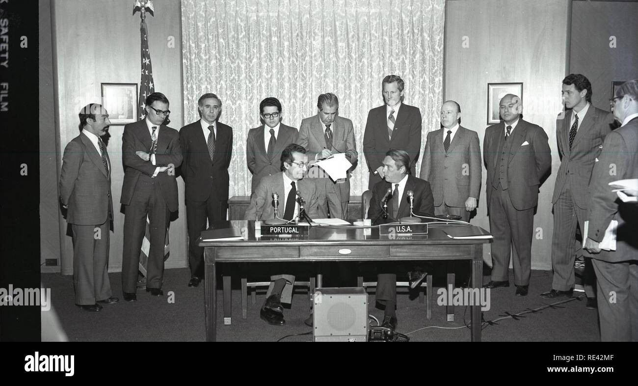 Gruppe von Männern; zwei standortwahl am Schreibtisch, die miteinander sprechen, mit einem Schild mit der Aufschrift PORTUGAL UND USA, als andere Männer. Stockfoto