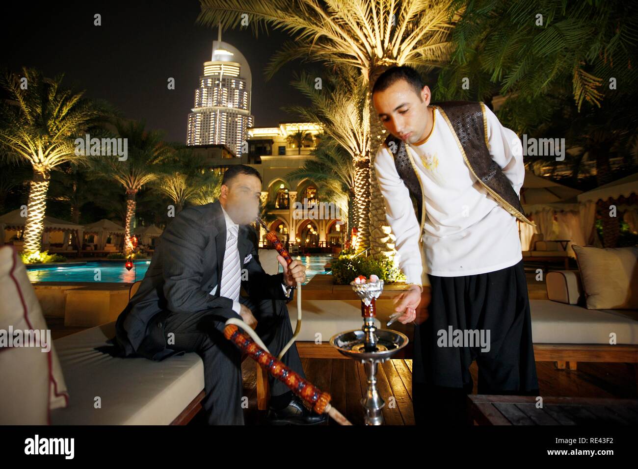 Mann Rauchen einer Wasserpfeife, Shisha, am Pool am Abend, das Palace Hotel, Altstadt, Dubai, Vereinigte Arabische Emirate, Naher Osten Stockfoto