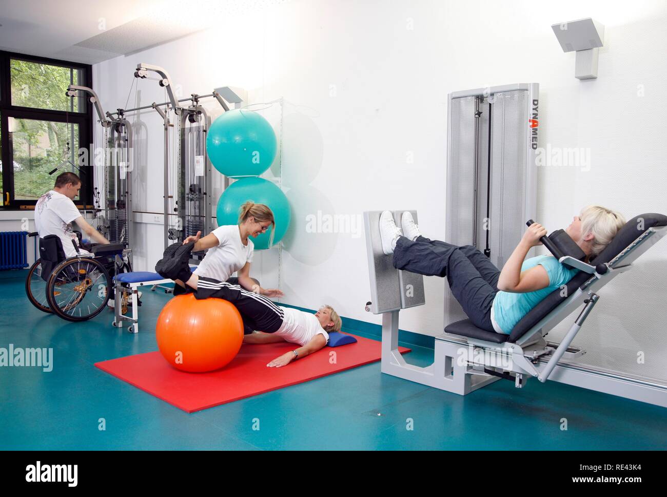 Patienten, die in den Muskeln Training auf verschiedenen Maschinen in einer Turnhalle, gymnastischen Übungen mit einer Therapie ball, Physiotherapie, Stockfoto
