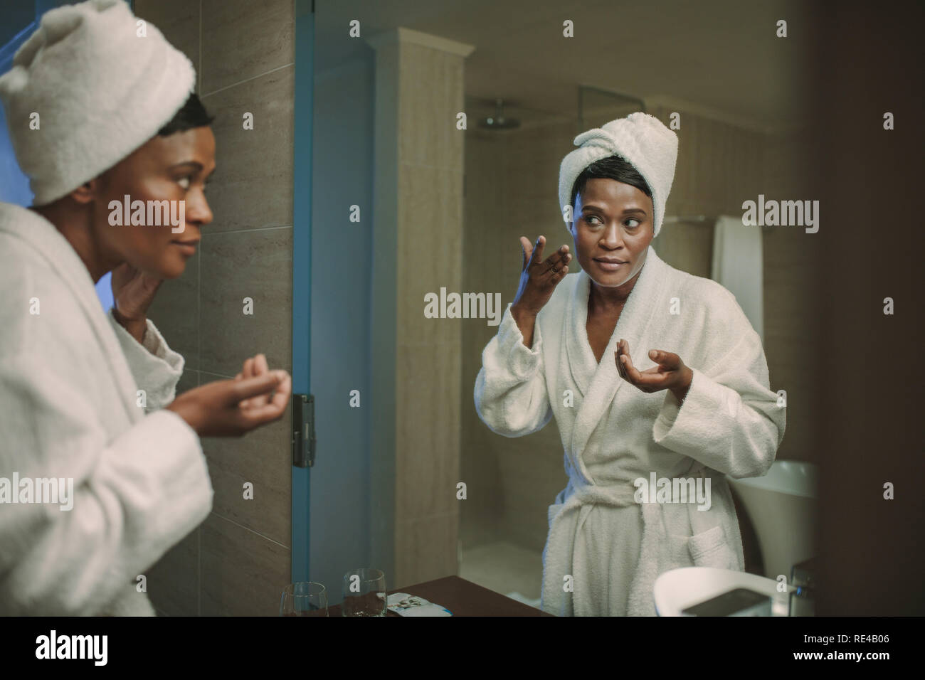 Afrikanische Frau Anwendung die Creme in Bad Spiegel nach Ihrer Badewanne. Frau kümmert sich um Ihre Haut und Gesicht Creme im Badezimmer. Stockfoto