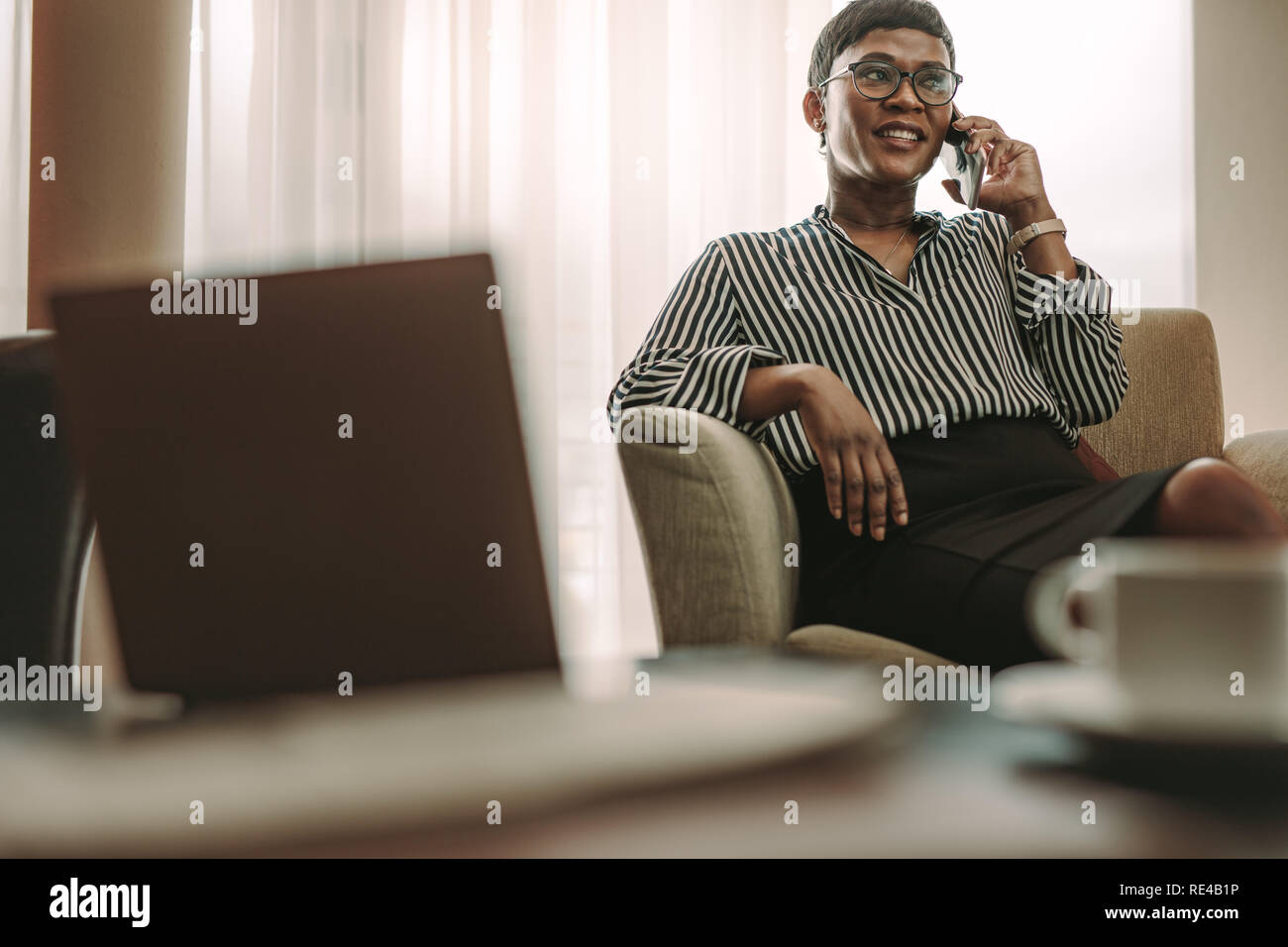 Happy Geschäftsfrau sitzt auf einem Sessel im Zimmer und Gespräch am Handy. Frau in formelle Kleidung Entspannung im Hotel Zimmer und Anruf. Stockfoto