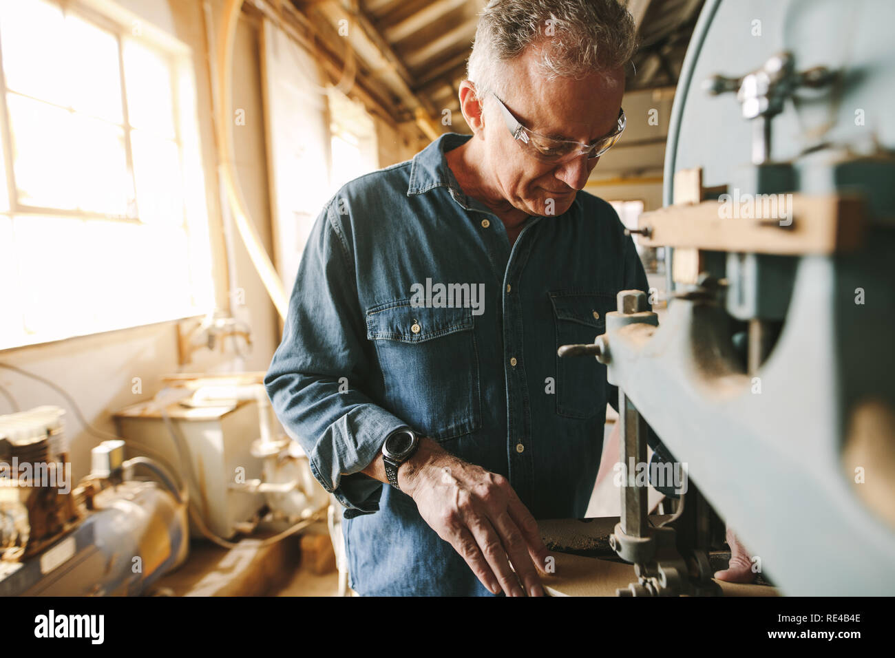 Ältere männliche Tischler arbeiten in seiner Werkstatt. Tischler Schneiden von Holz auf der Maschine in der Schreinerei. Stockfoto