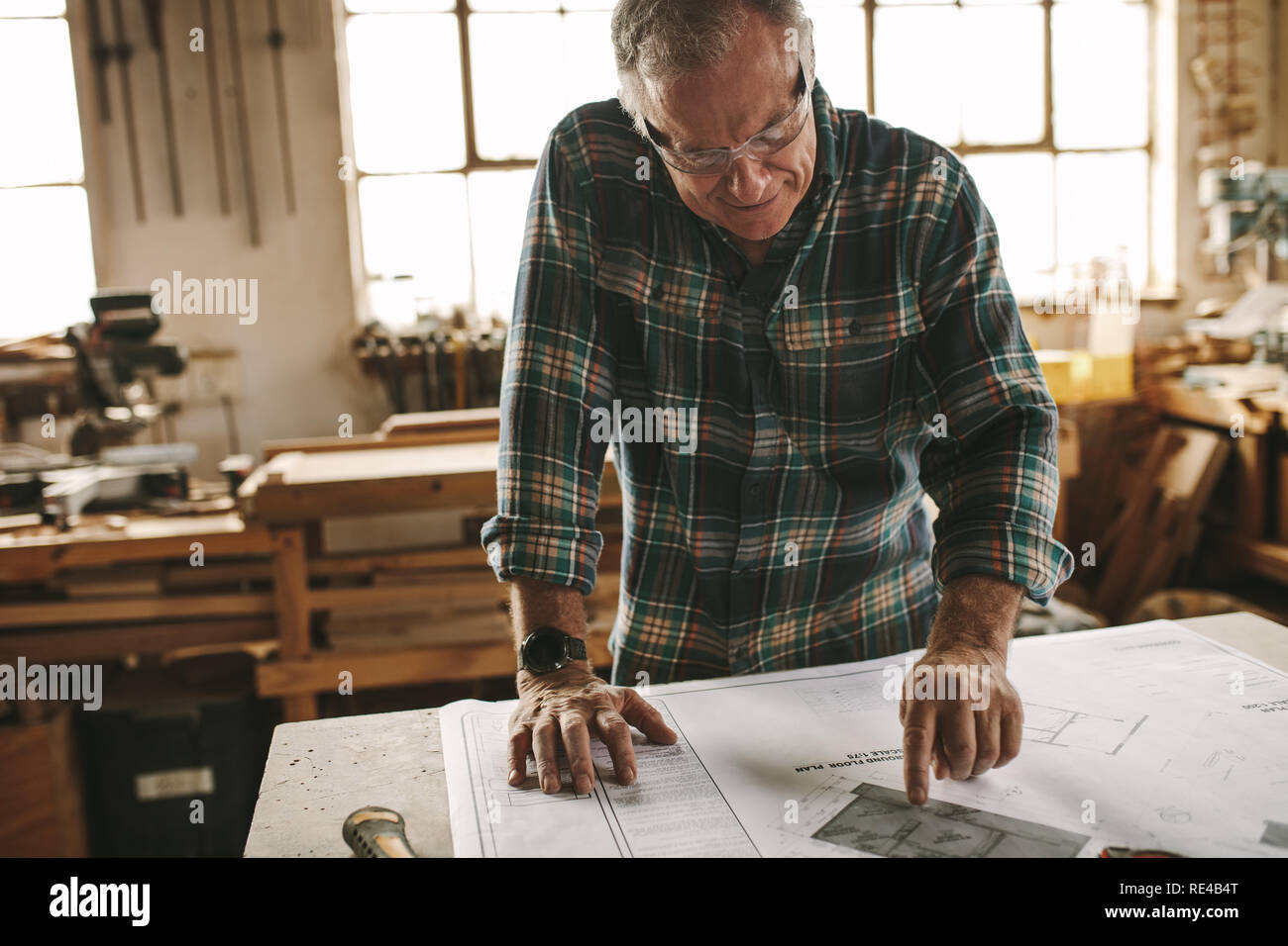 Senior Zimmermann Studium der Zeichnung vor dem Beginn seiner Arbeit am Workshop. Tischler Kontrolle Zeichnung in der Schreinerei. Stockfoto
