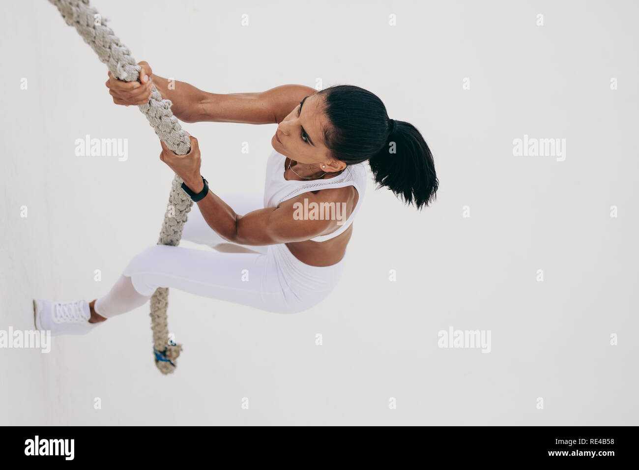 Ansicht von oben in eine athletische Frau klettern eine Wand mit einer Schlacht Seil. Frau tun Krafttraining klettern eine Wand mit einem Seil. Stockfoto