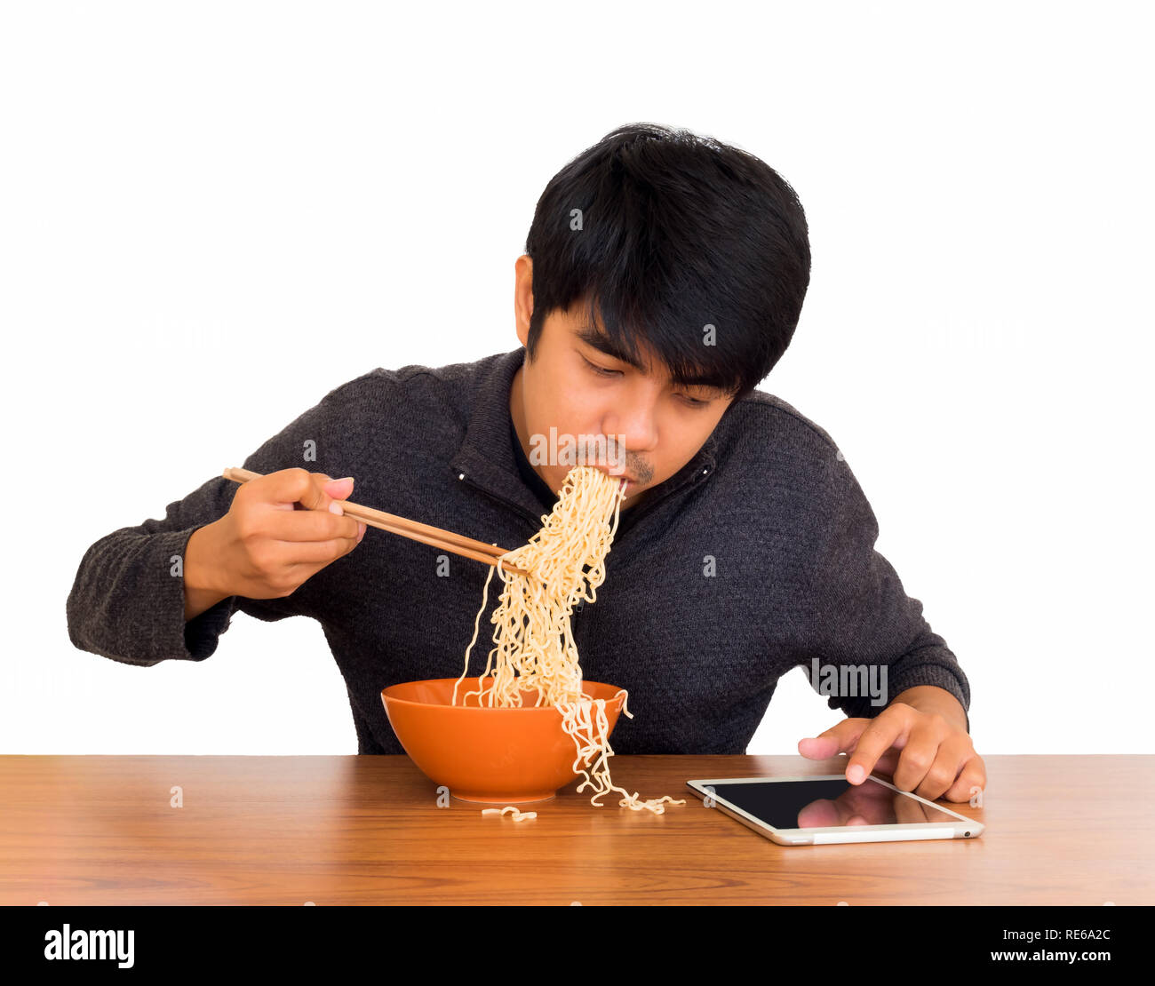 Mann essen chinesische Nudelsuppe monströs während der Suche und Verwendung von Tablet auf weißem Hintergrund mit Freistellungspfad isolieren. Konzept der Smartphone sucht, Stockfoto