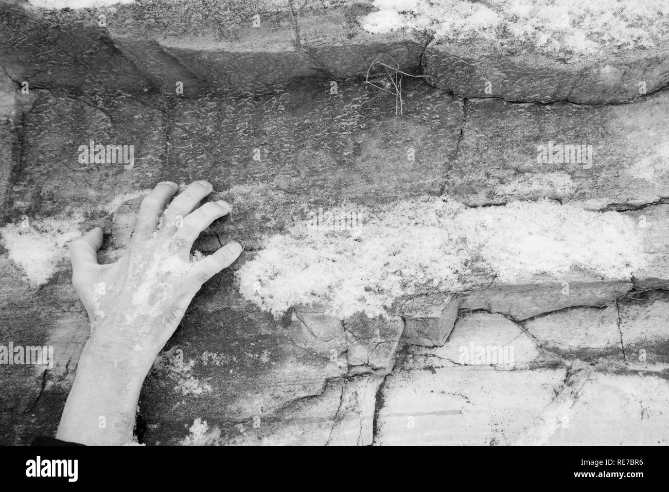 Die Hand eines Mannes klammert sich an einer Leiste auf einen Stein. Stockfoto