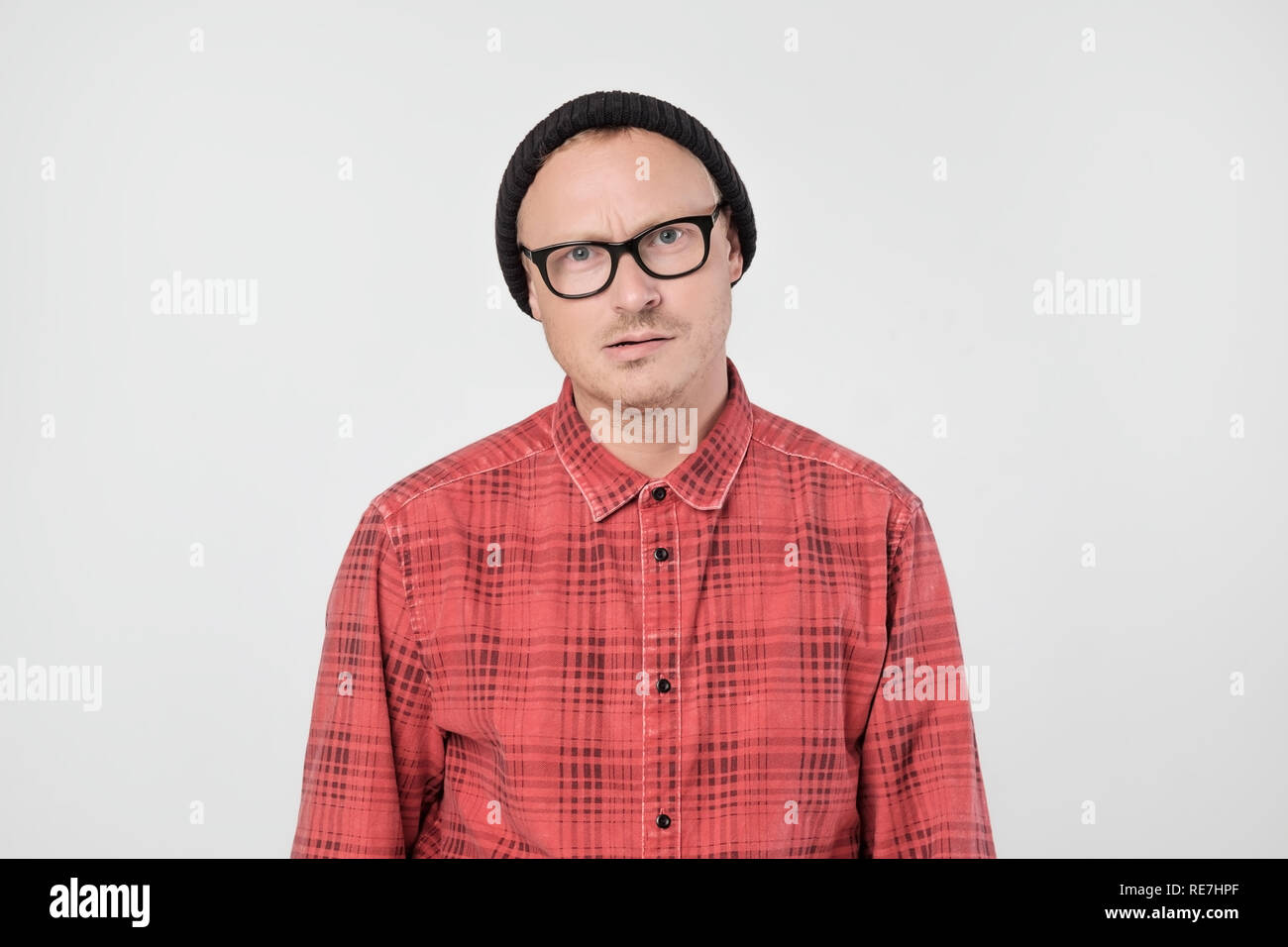 Junge europäische Mann im roten T-Shirt unzufrieden runzelt die Stirn und blickt missmutig. Stockfoto