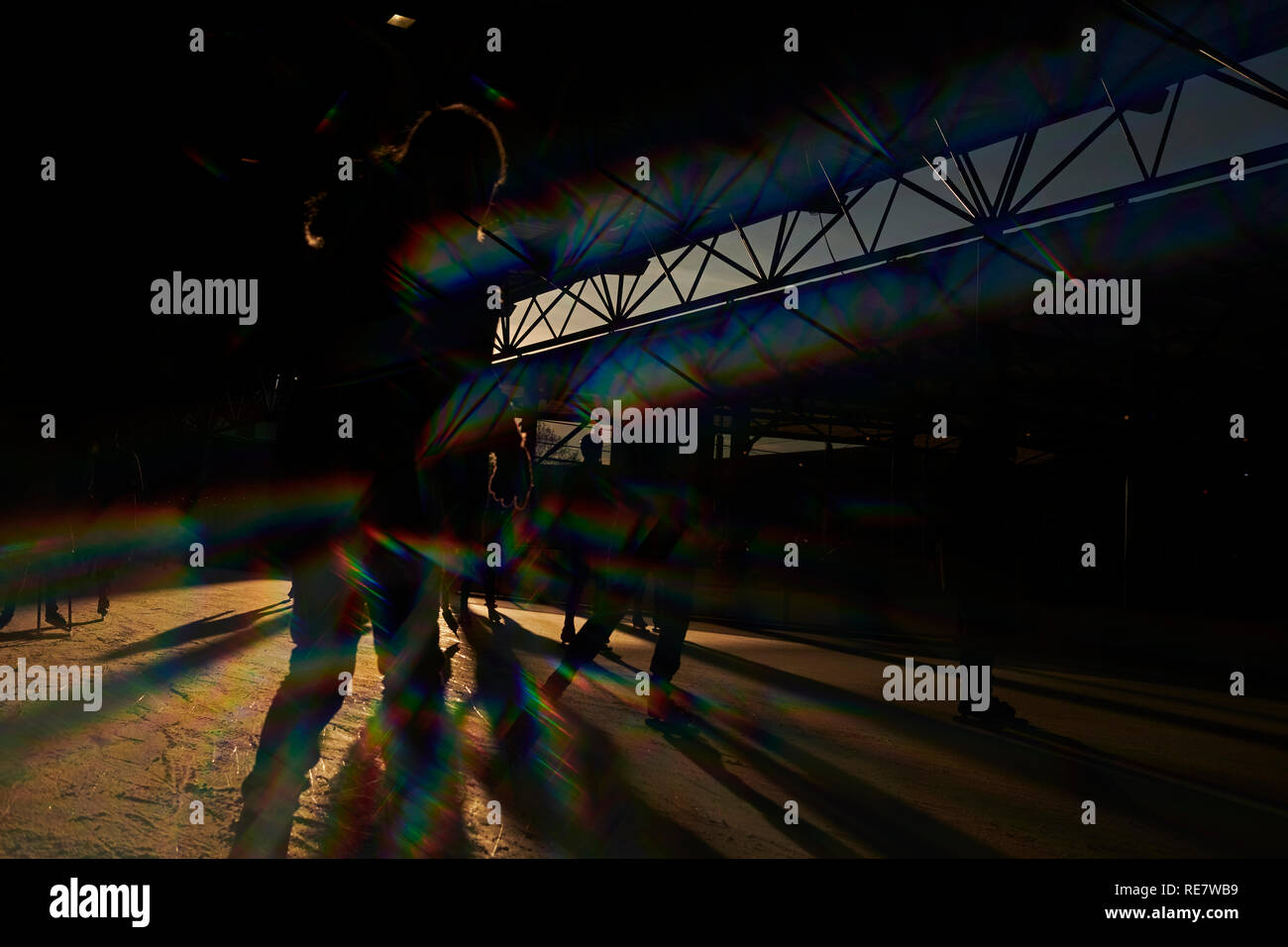 Massen von Menschen jung und alt Spaß Eislaufen im Winter Sonnenschein mit langen Schatten, Bewegung und Silhouetten Stockfoto