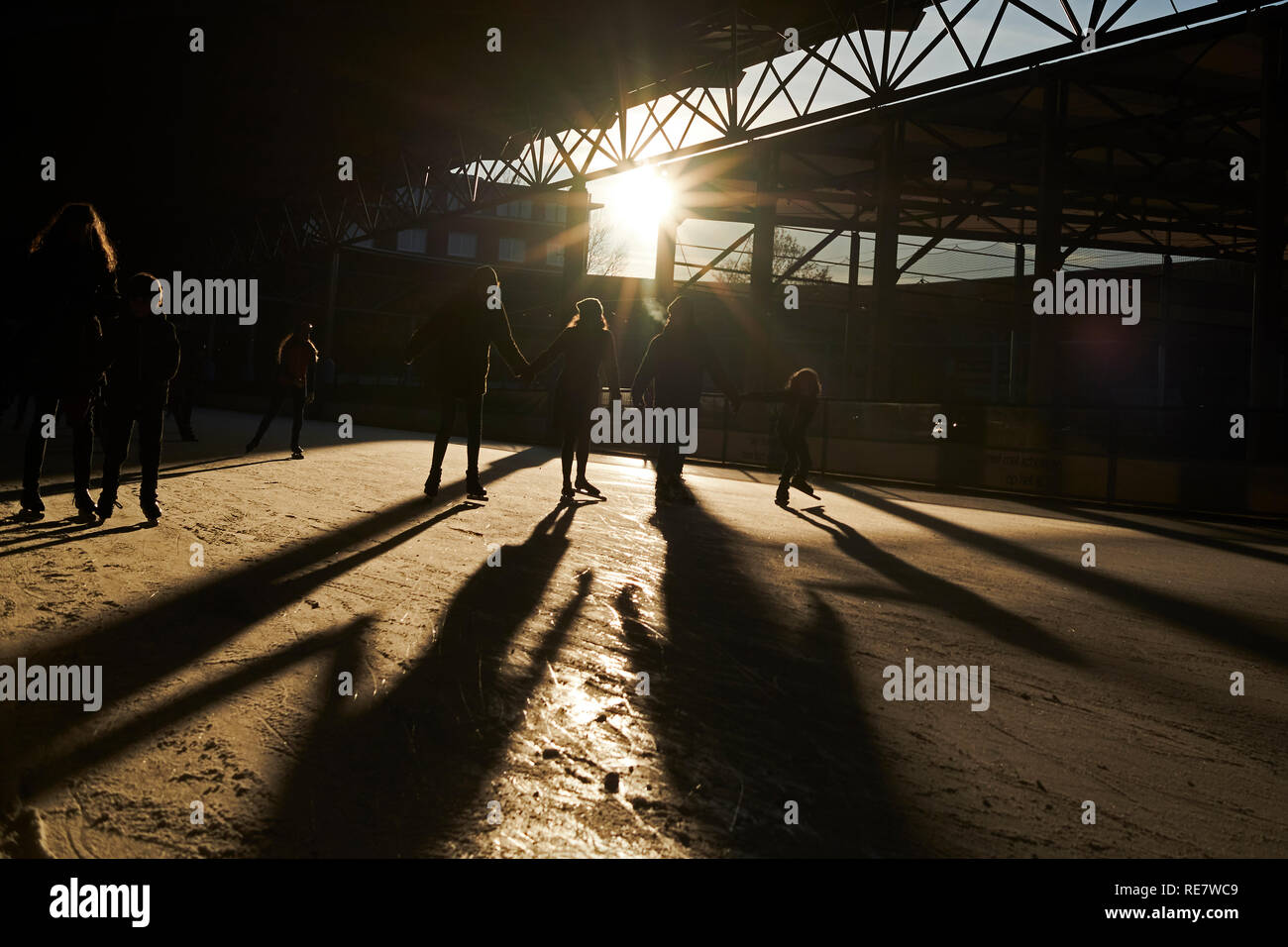 Massen von Menschen jung und alt Spaß Eislaufen im Winter Sonnenschein mit langen Schatten, Bewegung und Silhouetten Stockfoto