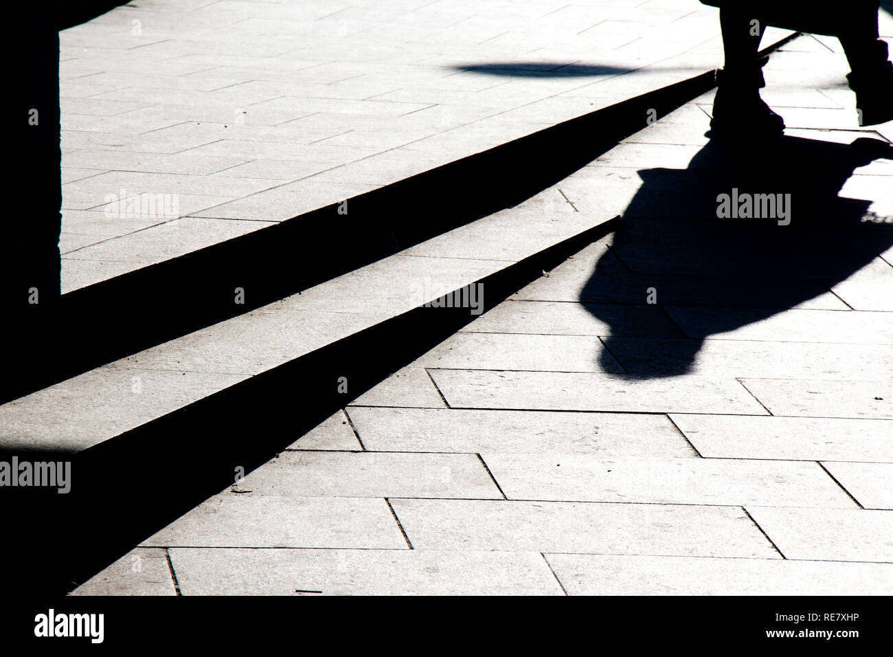 Unscharfe silhouette Schatten von einer Person zu Fuß auf eine Stadt Bürgersteig im Winter in Schwarz und Weiß mit hohem Kontrast Stockfoto