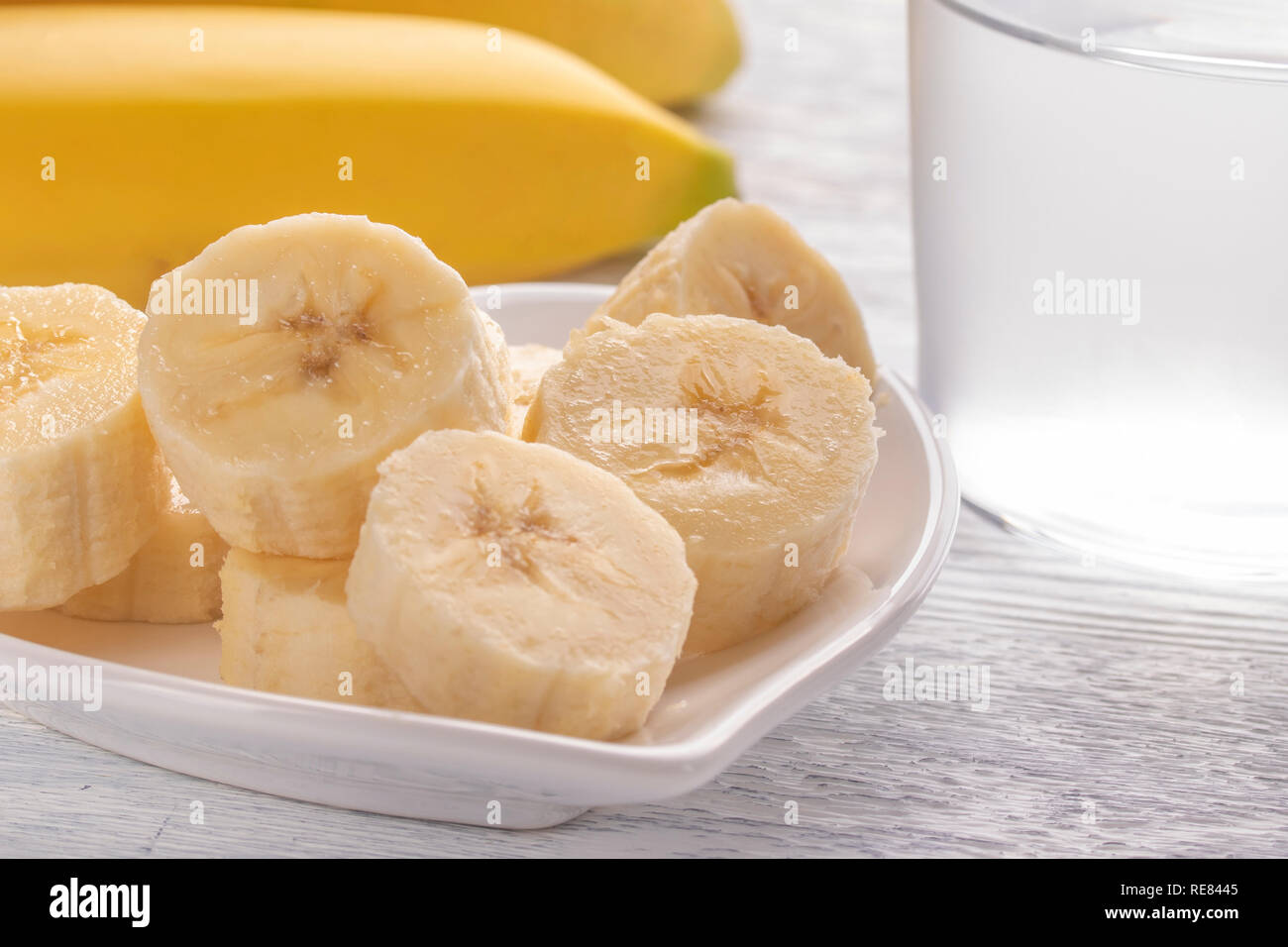 In Scheiben geschnitten und ganze Bananen. Auf einer weißen Platte. Auf dem alten Holztisch. Mit sauberem Wasser besprühen. Das Konzept der gesunden Ernährung und Verdauung. Stockfoto