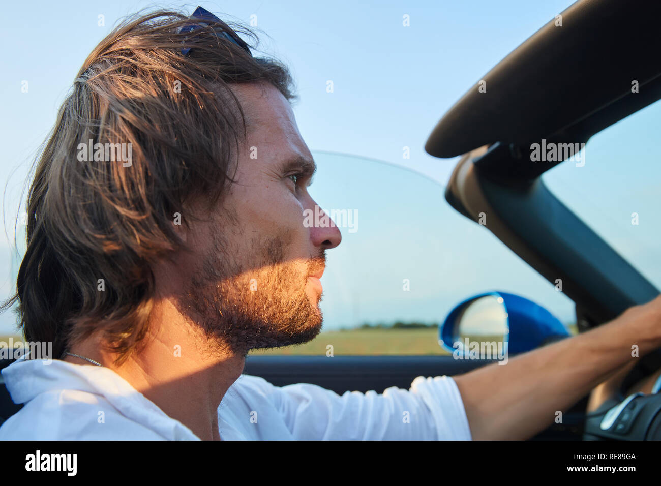 Die jungen brutalen Mann mit langen Haaren und Bart an einem Auto ohne Spitze, Cabriolet, blaue Farbe, Sonnenbrille Stockfoto