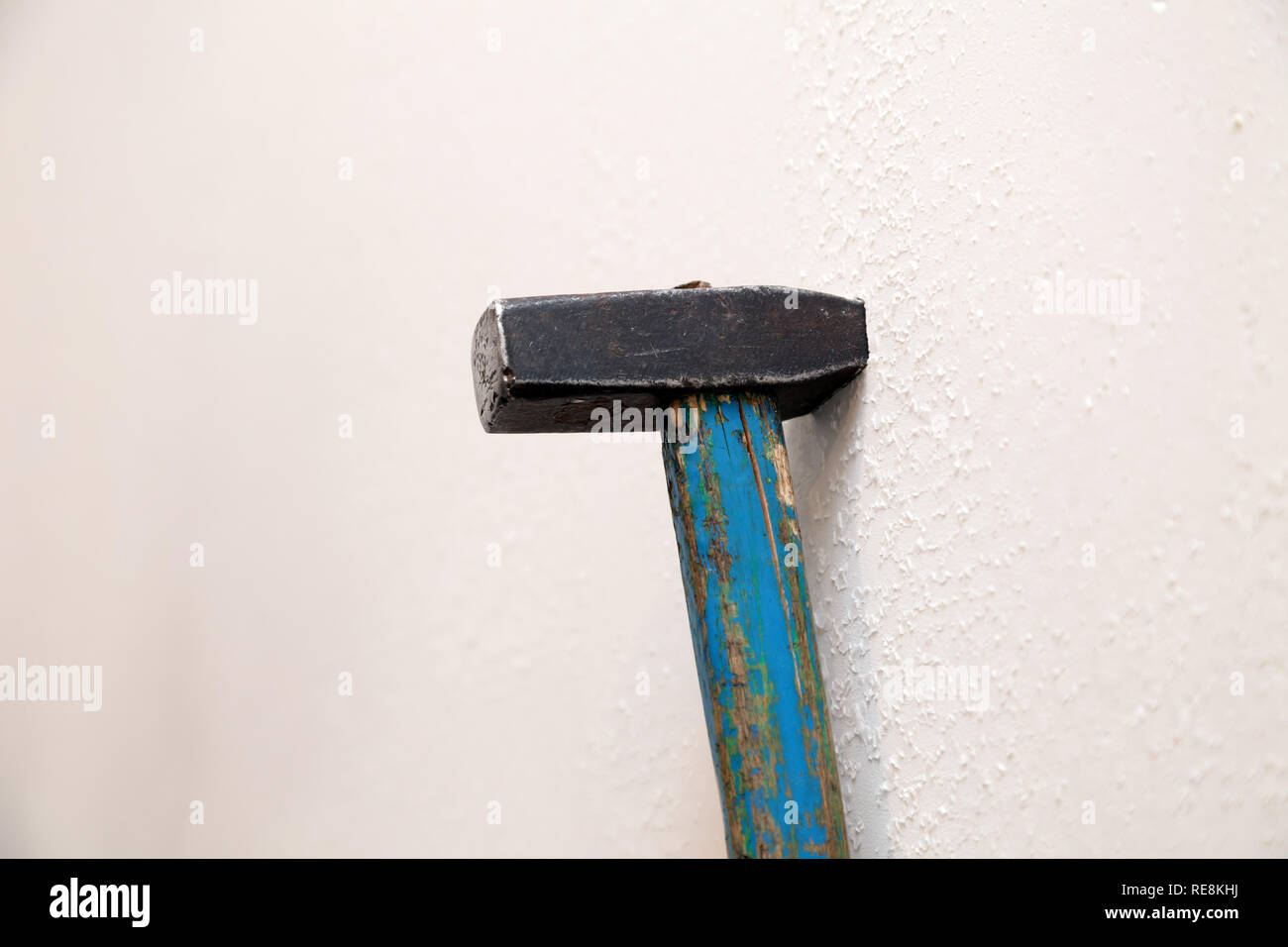 Nahaufnahme des alten Black Iron Hammer mit schäbigen blauen Griff aus Holz in eine weiße Wand hängen geblieben. Das Konzept der Reparatur, Sanierung, Umbau, restoratio Stockfoto