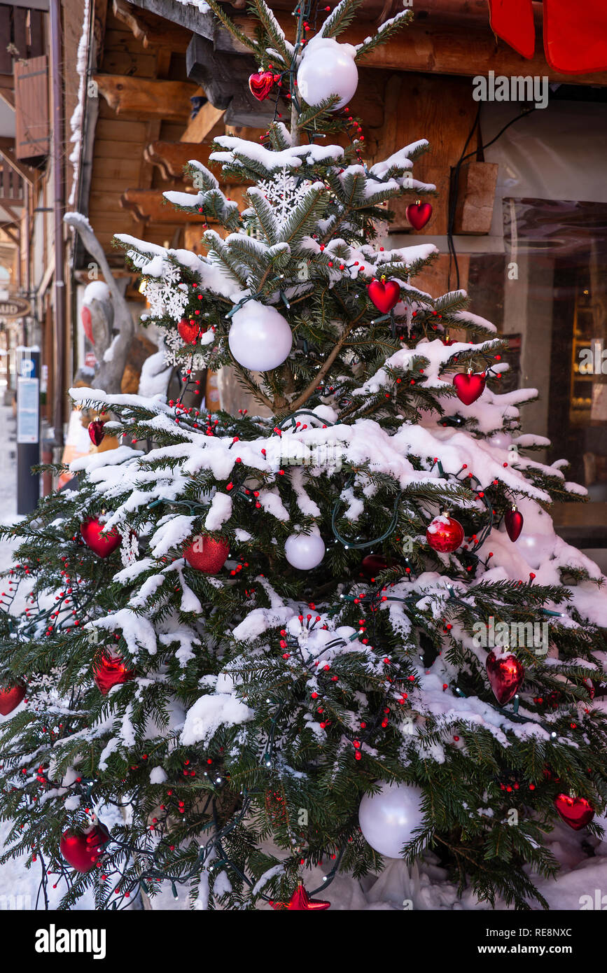 Ein großer Weihnachtsbaum mit roten Kugeln, Herz, Schnee und weisse kreisrunden Licht auf einer Straße in Morzine Haute Savoie Portes du Soleil Frankreich Stockfoto