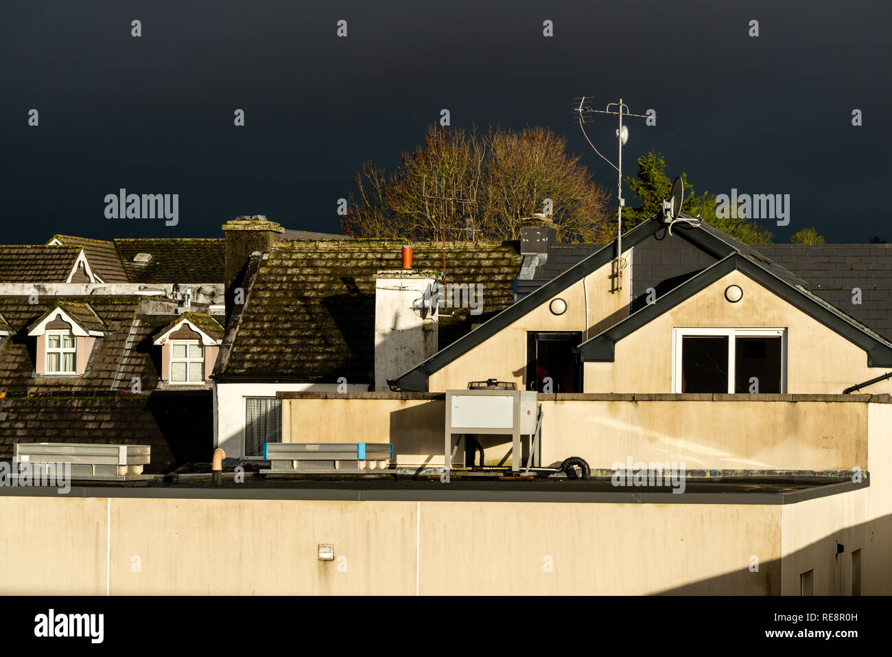 Sonnenbeleuchtete mossige Gebäudedächer und dramatischer stürmischer dunkler Himmel als urbane Infrastruktur und Nebeneinander, Irland Stockfoto