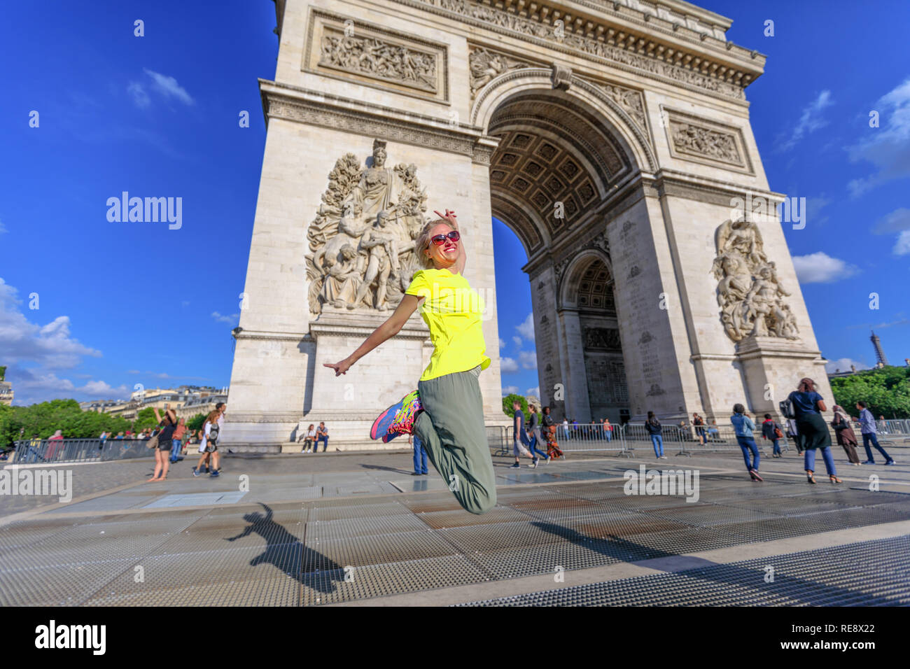 Frau mit gelber Weste am Triumphbogen springen. Beliebte Sehenswürdigkeiten in Paris, Frankreich. Konzept des Glücks für den Triumph der Proteste der Bevölkerung. Gilets Jaunes sind Symbol der Pariser Protestbewegung. Stockfoto