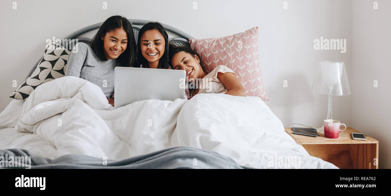 Drei Mädchen im Bett lag, in eine Decke ansehen Film auf einem Laptop. Mädchen Spaß mit einem Laptop auf dem Bett liegen, während ein sleepover. Stockfoto