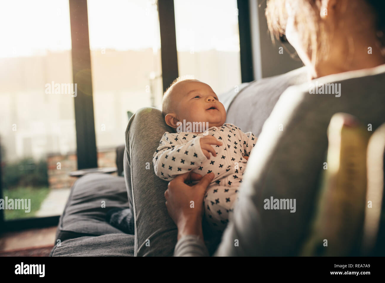 Blick über die Schulter der Mutter mit ihrem Kind auf einer Couch zu Hause. Rückansicht eines Mutter spielt mit ihrem Baby mit Sun Flair in der Stockfoto