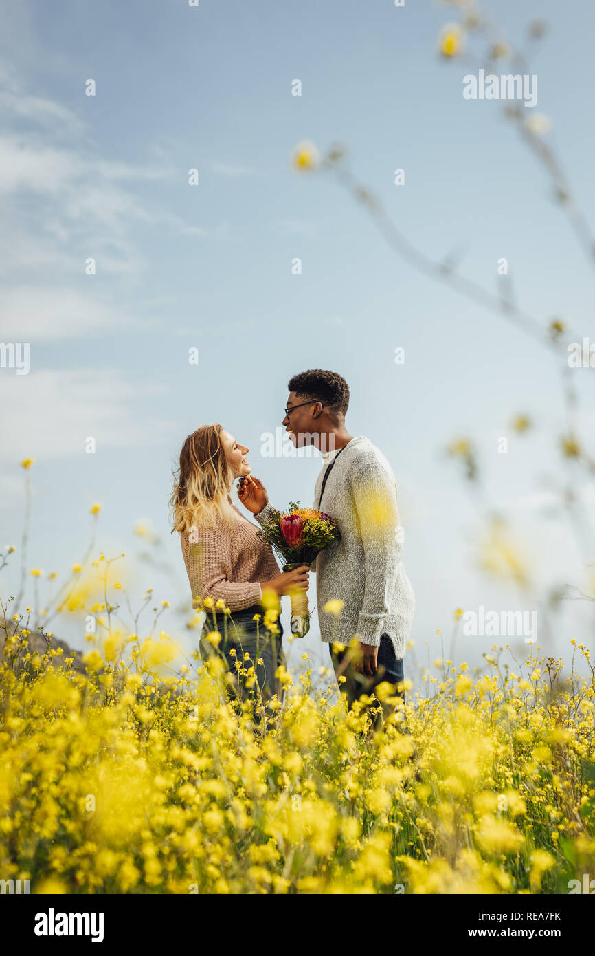 Seitenansicht des jungen Mannes an seine Freundin mit Blumen im Freien suchen. Interracial Paare zusammen und stehen einander mit der Liebe. Stockfoto