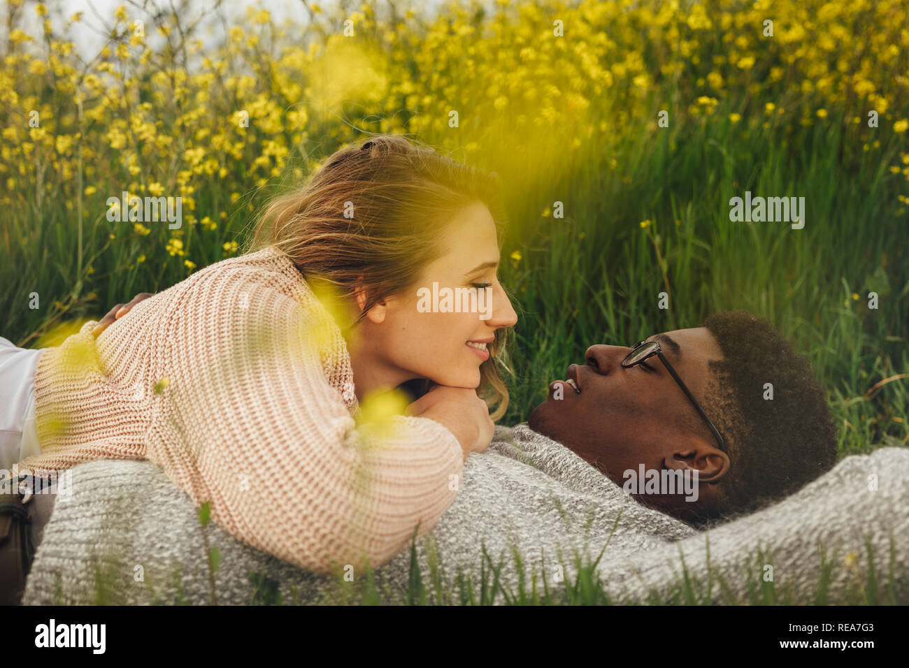 Junge Frau auf ihrem Freund im Freien. Junge multi-ethnischen Paar, die auf dem Gras in der Wiese und schauen in den Augen der anderen. Stockfoto