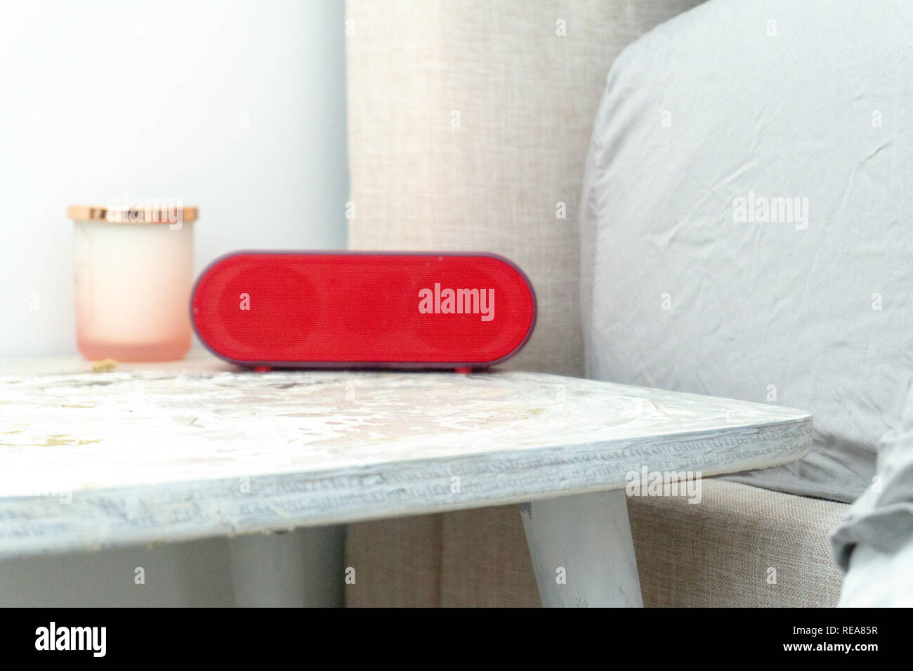 Leuchtend rote Radio Wecker und Candle jar auf den Nachttisch Nachttisch, mit Bettwäsche und Handtücher, in sanften Farben. Stockfoto
