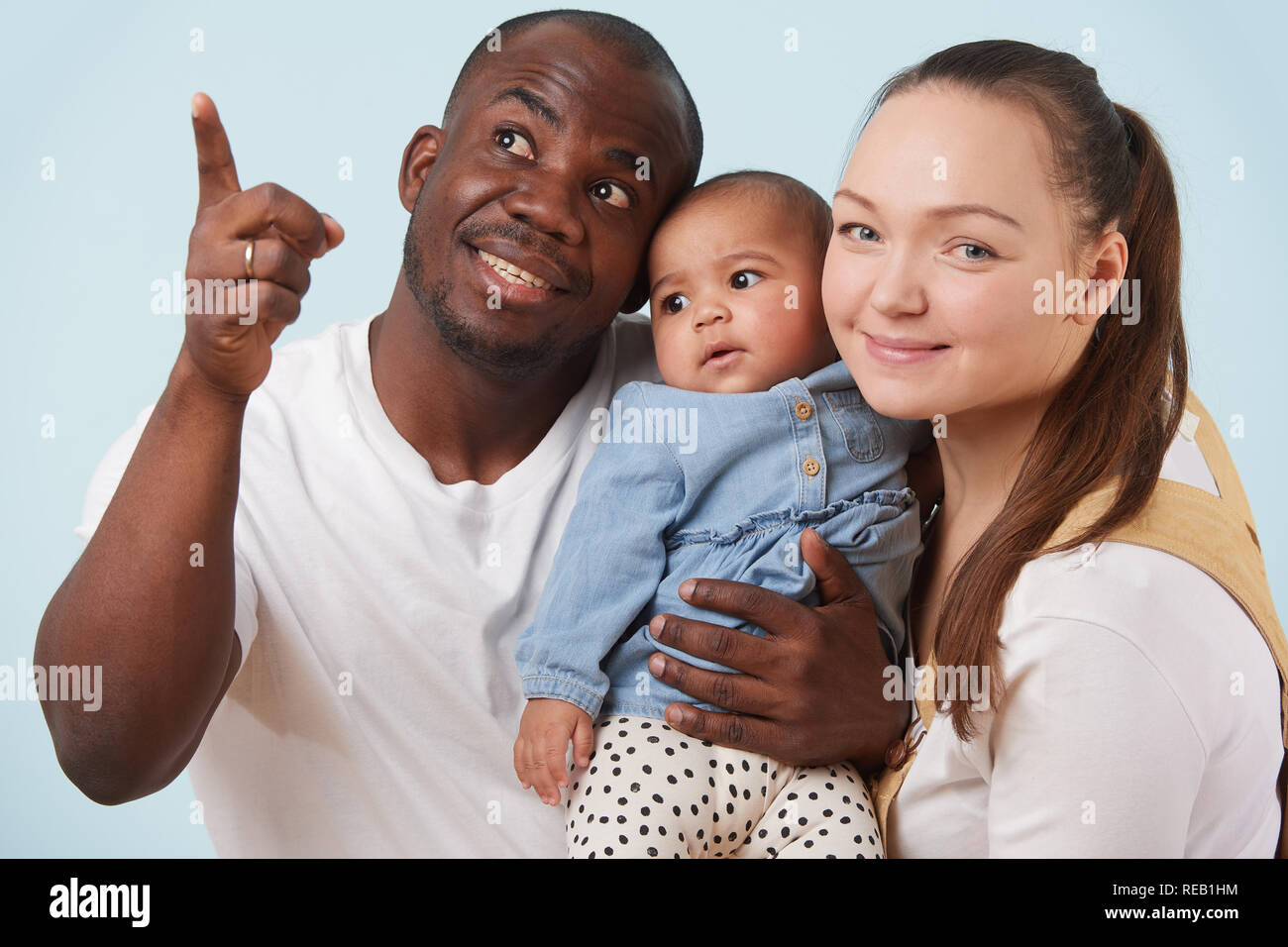 Portrait von Happy multiethnischen Familie: weiße Mutter, schwarz Vater und ihre kleine Tochter gemeinsam gegen blass blauen Hintergrund. Schließen Stockfoto