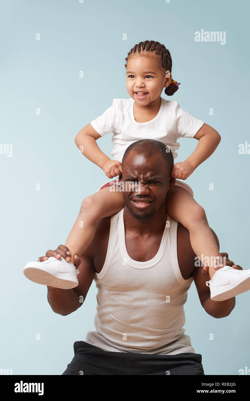 Stattlichen schwarzen Jungen Vater tut hockt mit seinem süßen kleinen Tochter ihn reiten. Er hat Probleme mit zusätzlichem Gewicht, der lustig ist zu h Stockfoto