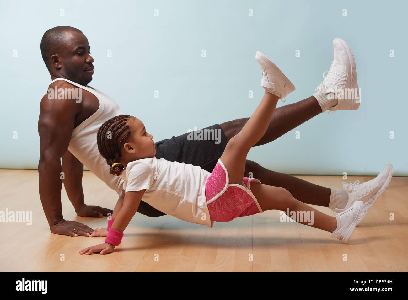 Stattlichen schwarzen jungen Vater und seine süsse kleine Tochter tun reverce Plank mit Bein anheben, auf dem Boden zu Hause. Familie Fitness Training. Stockfoto