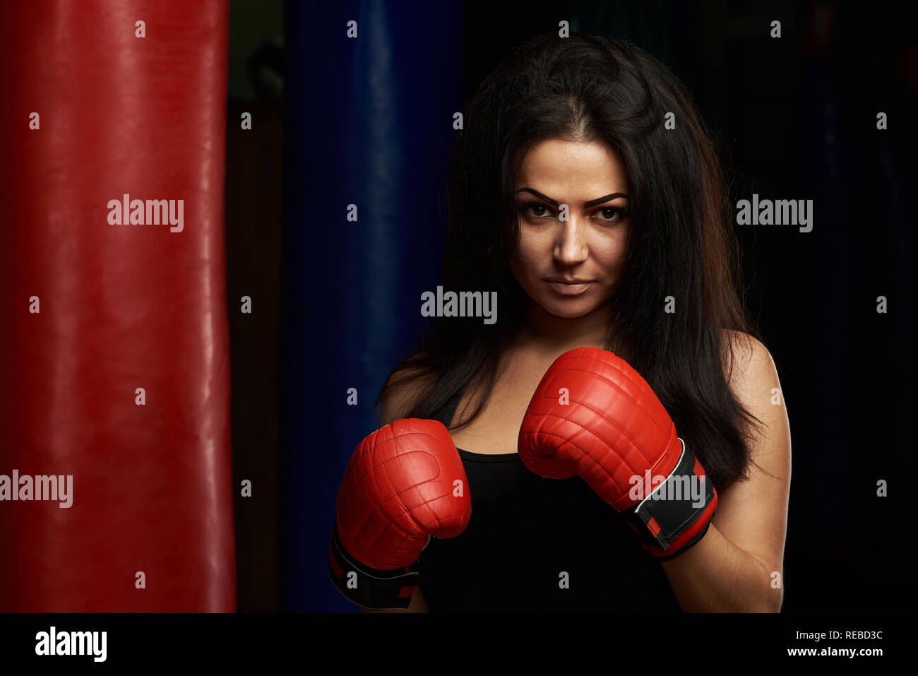Ernsthafte junge Frau mit Boxhandschuhen auf modernen Fitnessraum Hintergrund Stockfoto