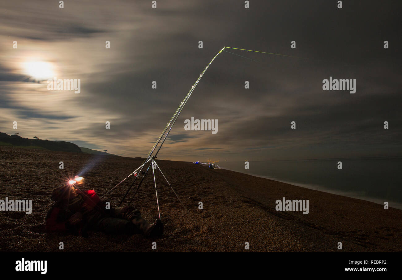 Eine lange Exposition von einem Angler in der Nacht mit einem Scheinwerfer Angeln am Chesil Beach in Dorset. Andere Angler können im Hintergrund gesehen werden. Die super Blut Stockfoto