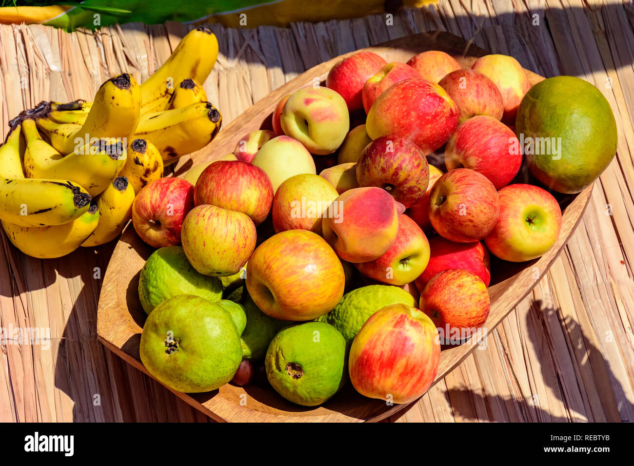 Hölzerne Schüssel und rustikalen Strohmatte mit verschiedenen Guaven, Äpfel und Bananen, die unter der Sonne Stockfoto