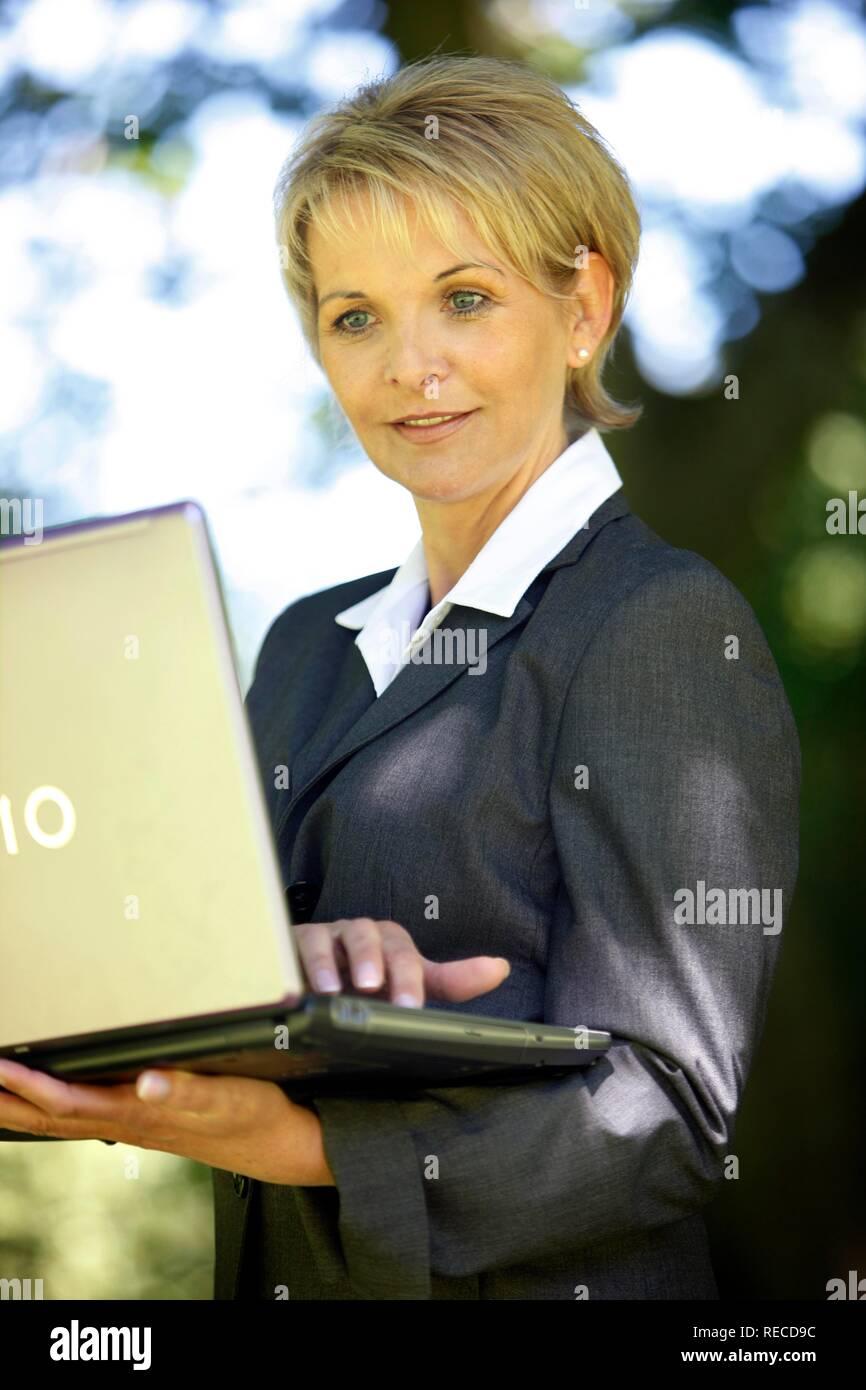 Frau trägt einen Anzug, Damen Hosenanzug, Geschäftsfrau, Anfang 40, arbeitet sie an ihrem Laptop in einem Park Stockfoto