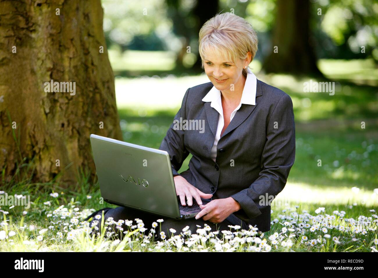 Frau trägt einen Anzug, Damen Hosenanzug, Geschäftsfrau, Anfang 40, arbeitet sie an ihrem Laptop in einem Park Stockfoto