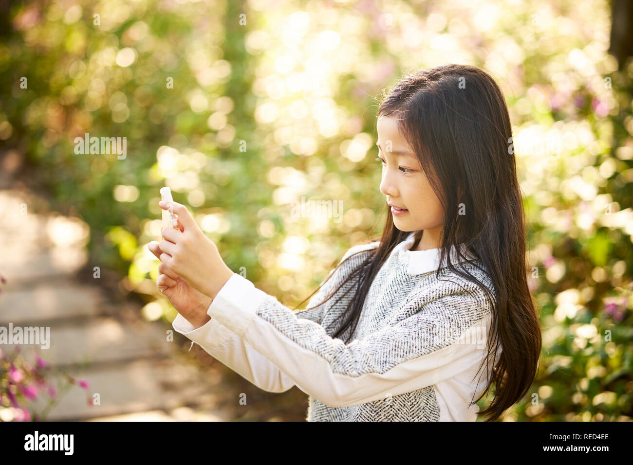 Schönen kleinen asiatischen Mädchen mit langen Haaren ein selfie gegen Blume Hintergrund mit Handy Stockfoto