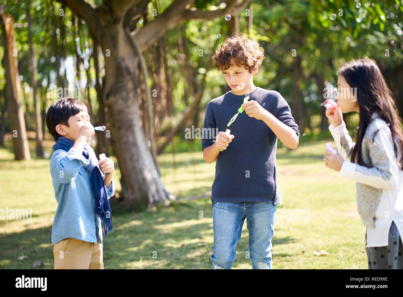 Zwei asiatische und italienische Kinder im Freien spielen im Park Seifenblasen Stockfoto