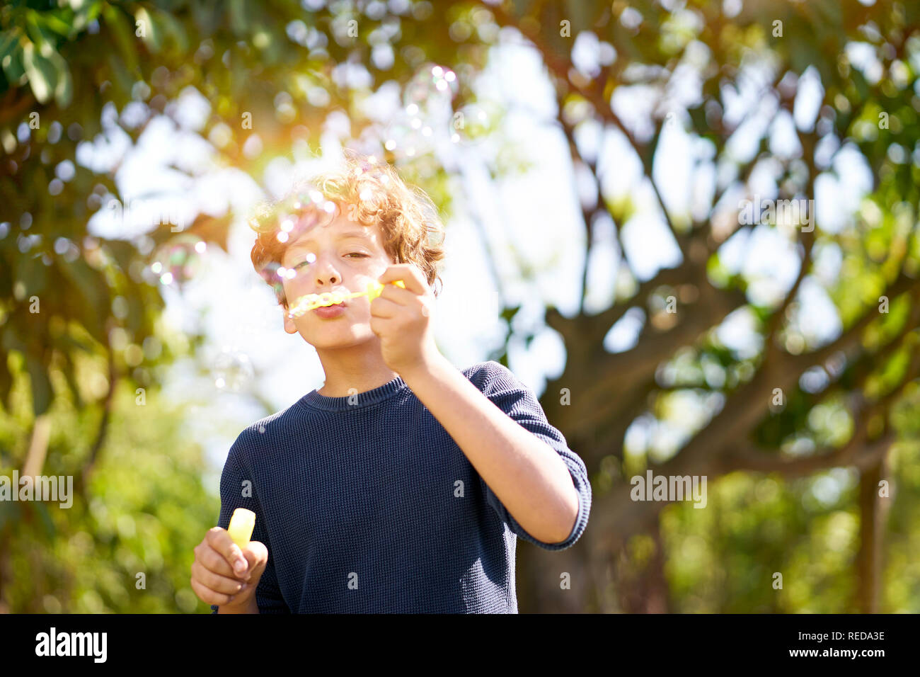 10-jährige italienische Junge bläst Seifenblasen draußen im Park. Stockfoto