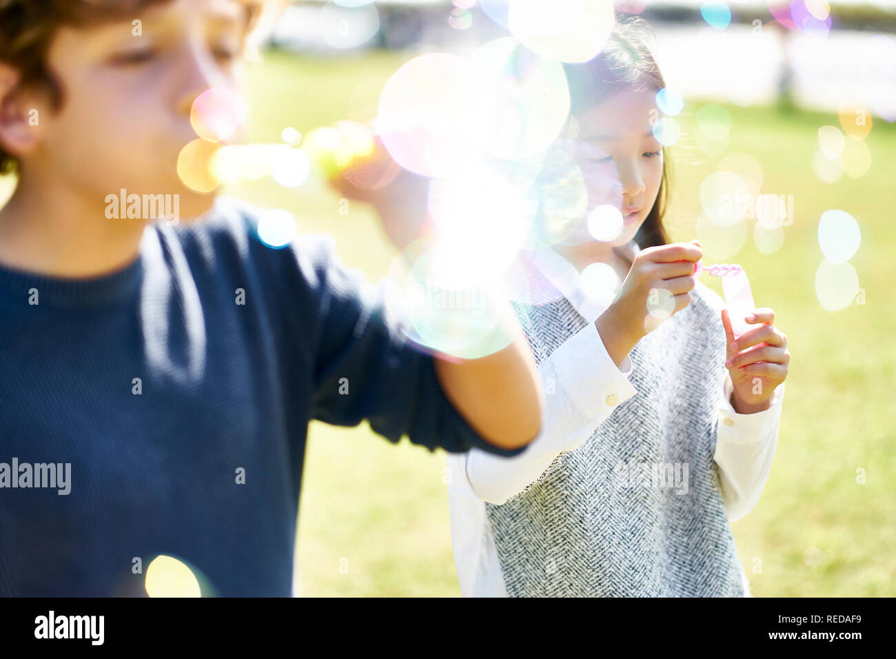 Wenig asiatisches Mädchen und kaukasischen Jungen zusammen spielen bläst Seifenblasen im Freien in einem Park. Stockfoto