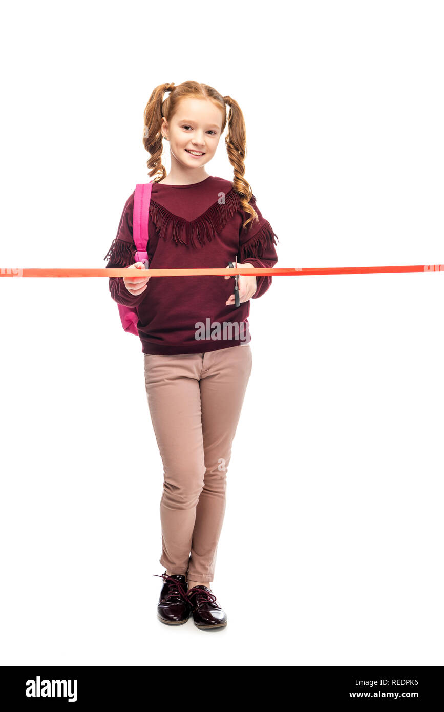 Lächelnd Schulmädchen mit rosa Rucksack schneiden Red Ribbon und Kamera isoliert auf weißem Stockfoto