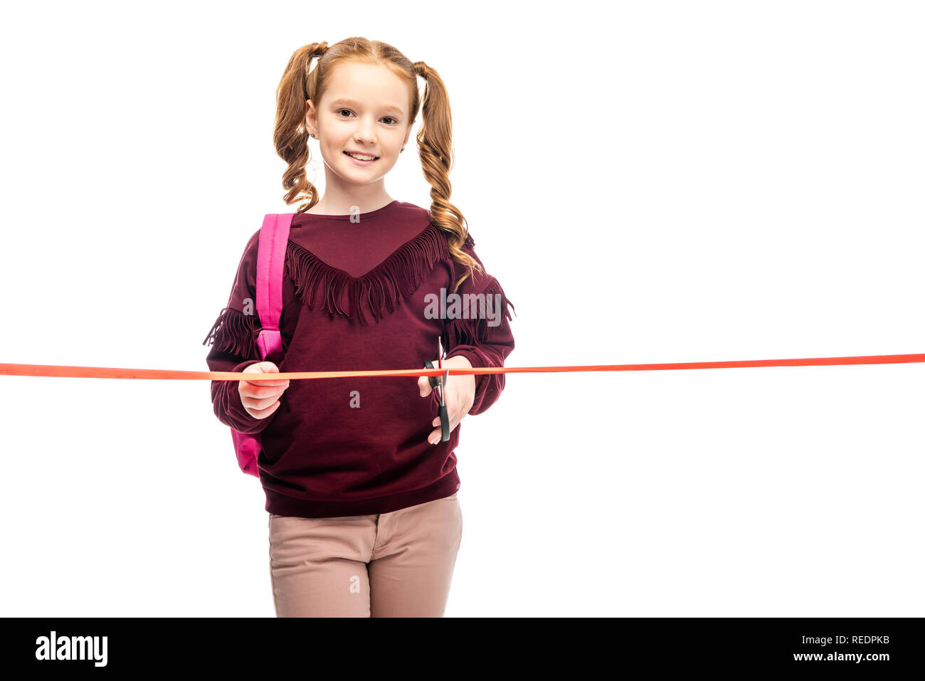 Lächelnd Schulmädchen schneiden Red Ribbon und Kamera isoliert auf weißem Stockfoto