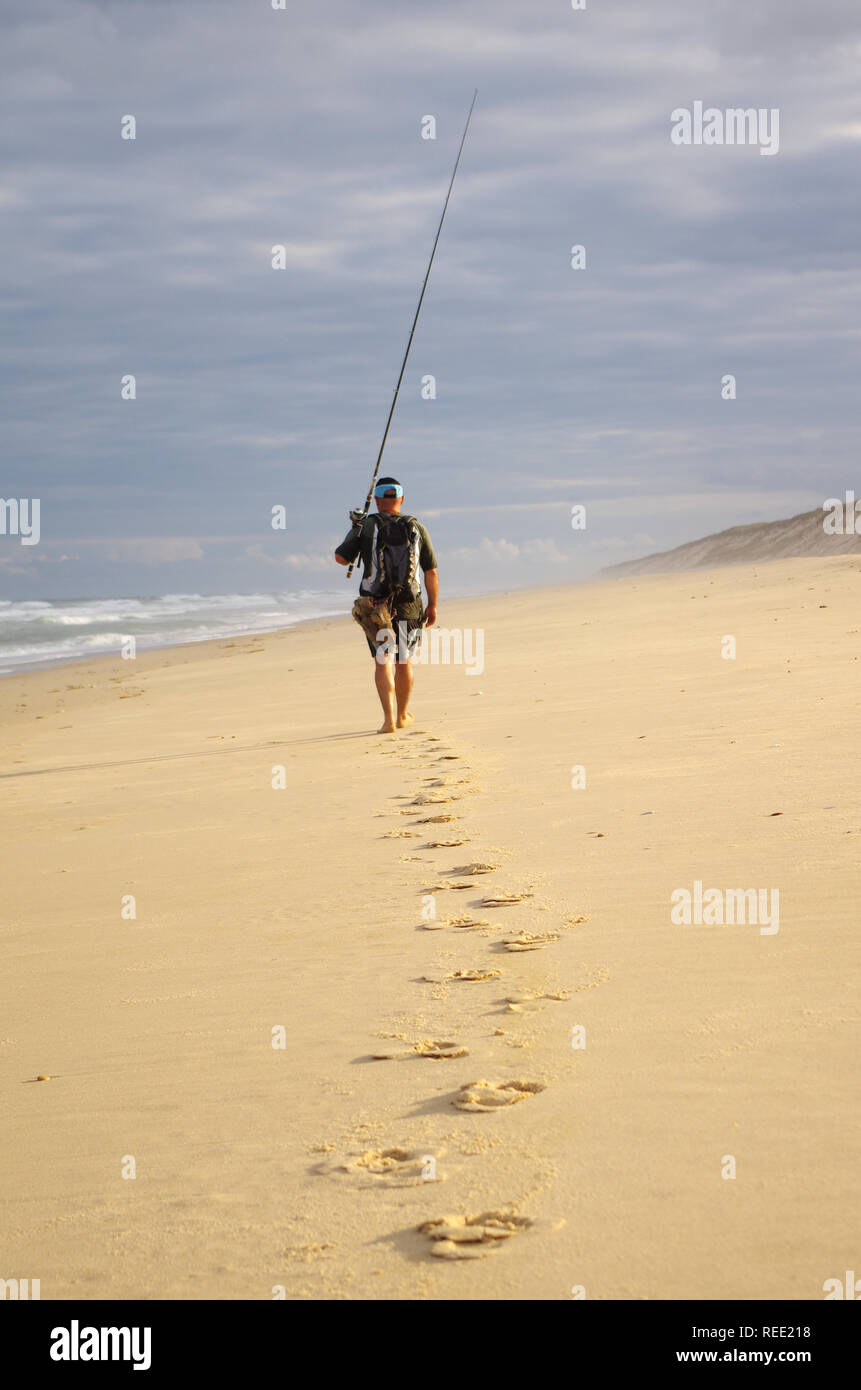 Surf Fischer mit seiner Angelrute zu Fuß in den Sand am Strand des Atlantik. Abenteuer, Angeln, wilde Fischerei Stockfoto