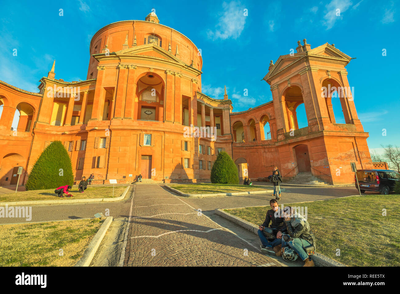 Bologna, Italien - 12 Januar, 2018: Romantisches Paar sitzen auf den Innenhof der Madonna di San Luca Heiligtum an einem sonnigen Tag. Zentrale Fassade der Basilika Kirche von San Luca. Das Wahrzeichen der Stadt. Stockfoto