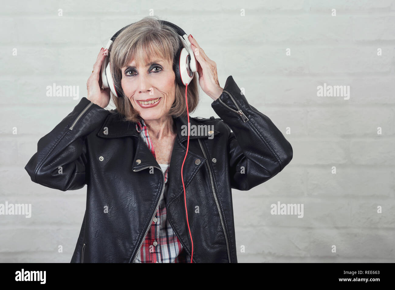 Lächelnde ältere Frau mit Kopfhörer Musik hören auf Stein Hintergrund Stockfoto