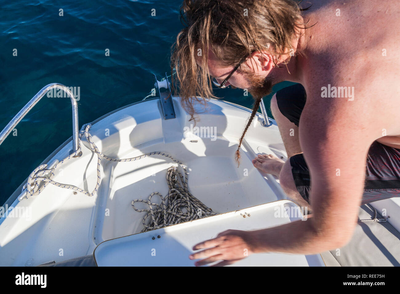 Ein junger Mann auf einem Boot Ziehen am Seil eines Ankers Stockfoto